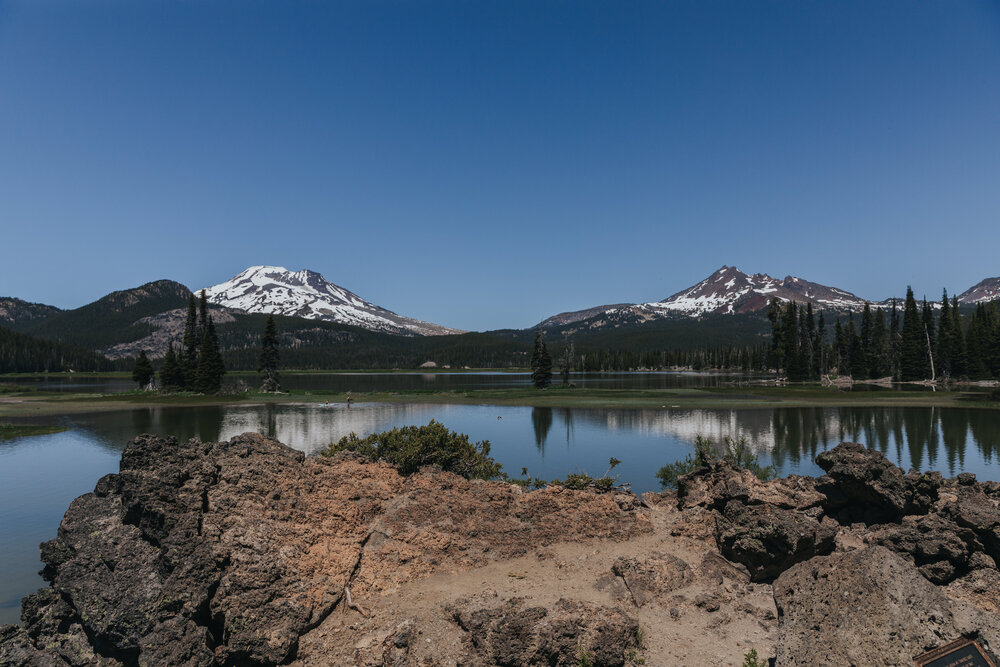 Pictured here is a view of the accessible paved path of the Ray Atkeson Trail at Sparks Lake. South Sister and Broken Top Mountains are visible from the path. This can be a great location option for an ADA-accessible elopement.