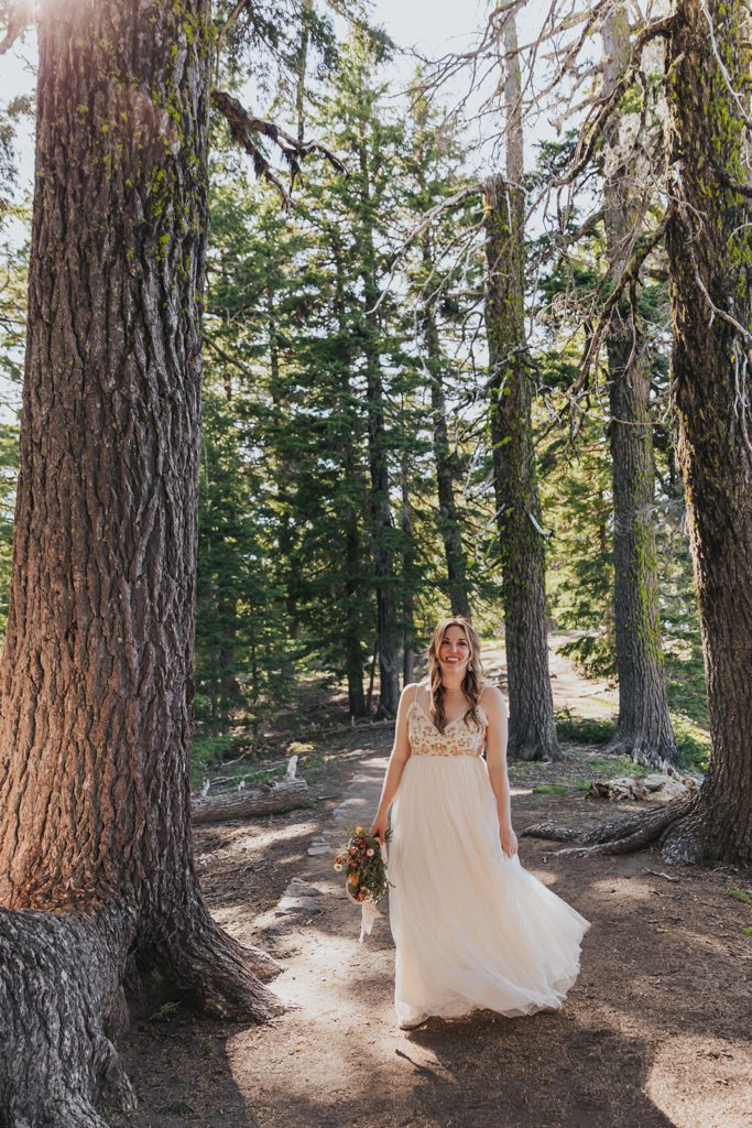 A bride is standing in a forest, wearing an embroidered tulle dress on her wedding day. This is one of the many examples of an affordable elopement dress featured in this blog post!