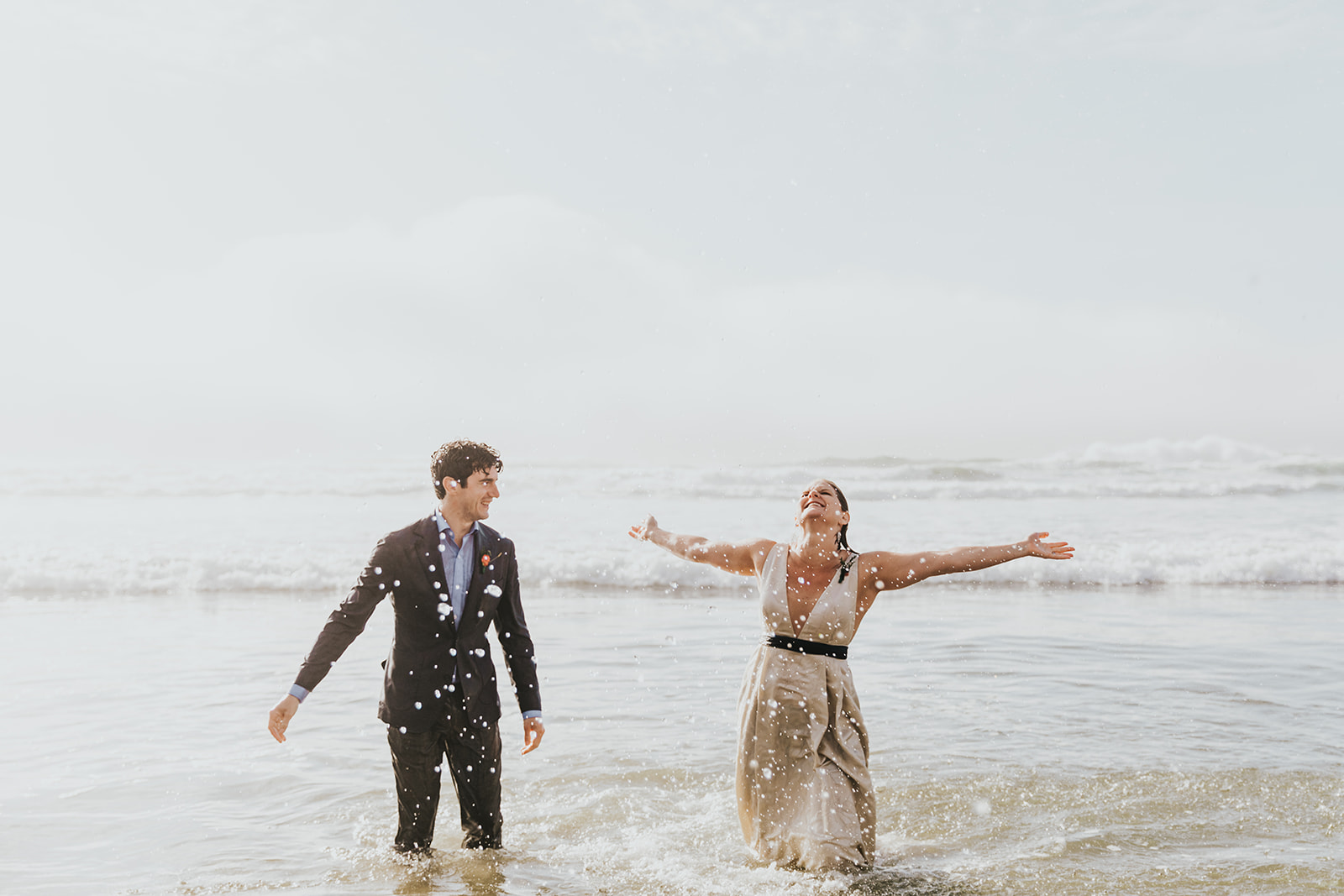 should we elope - a couple smiles as they play in the ocean in their elopement outfits