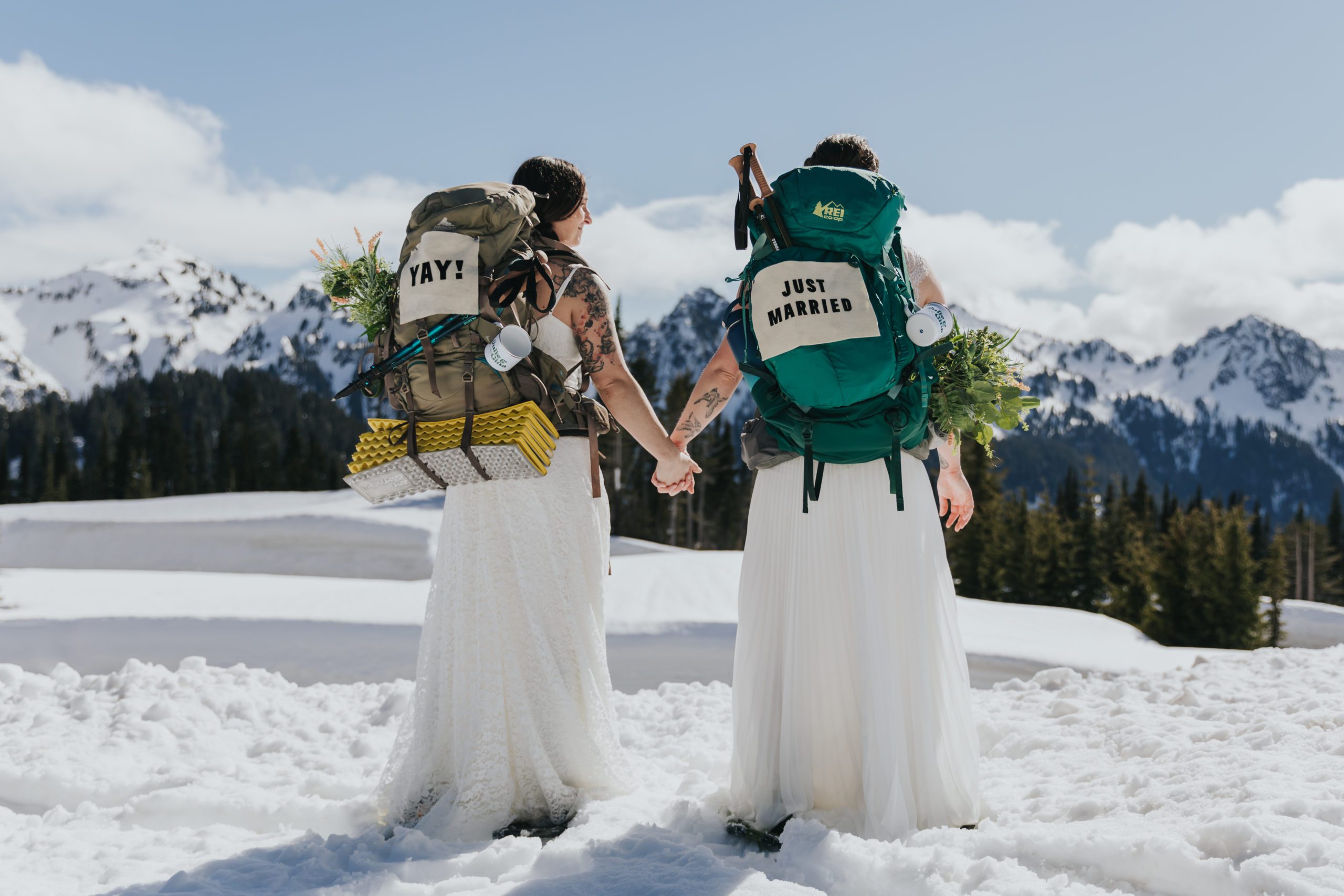 should we elope - a couple holds hands while wearing backpacks on their elopement day on a snowy mountain 