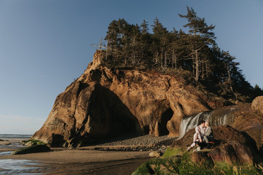 A couple kisses on a rock in front of Hug Point Waterfall - a great Northern Oregon Coast Elopement Location! 