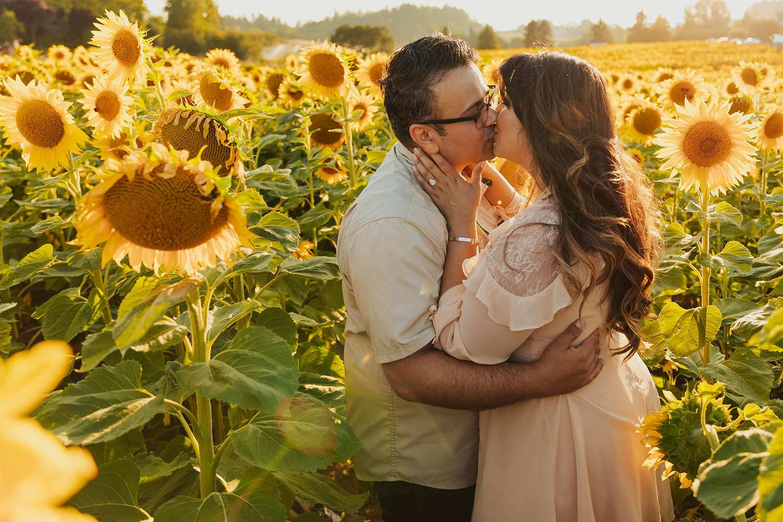 A couple kisses in a sunflower field at West Union Gardens for their engagement photo shoot, a popular engagement photo location near Portland. 