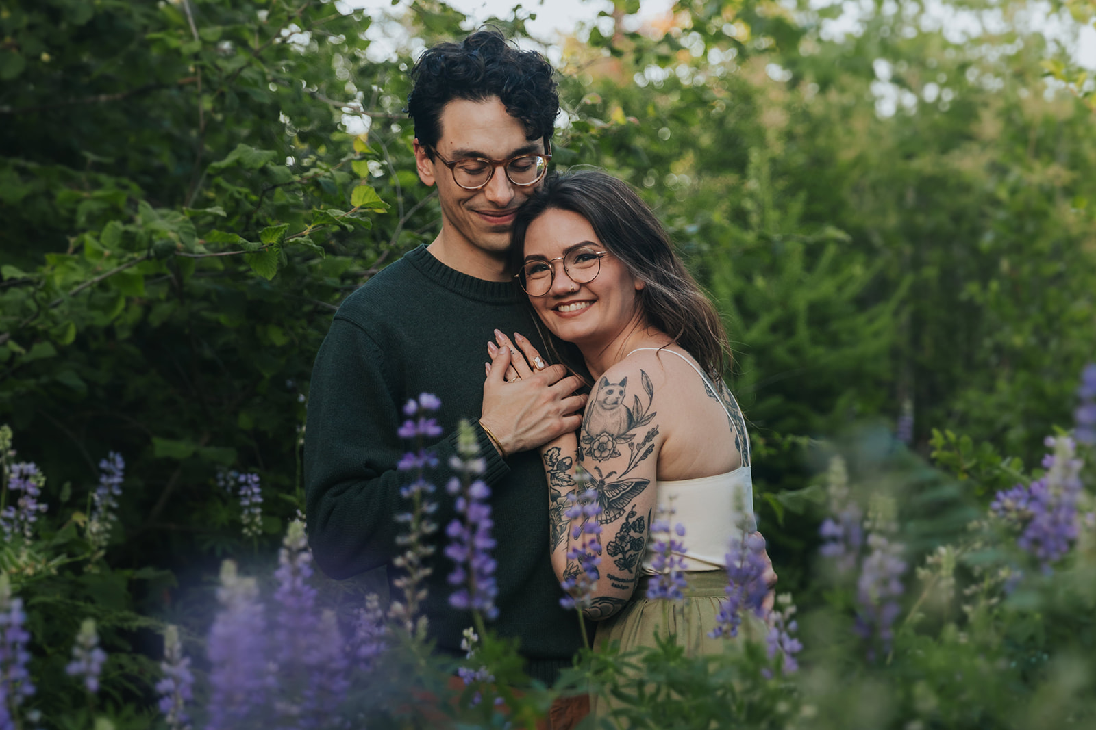 A man and woman are cuddling together in a lupine field for their engagement session