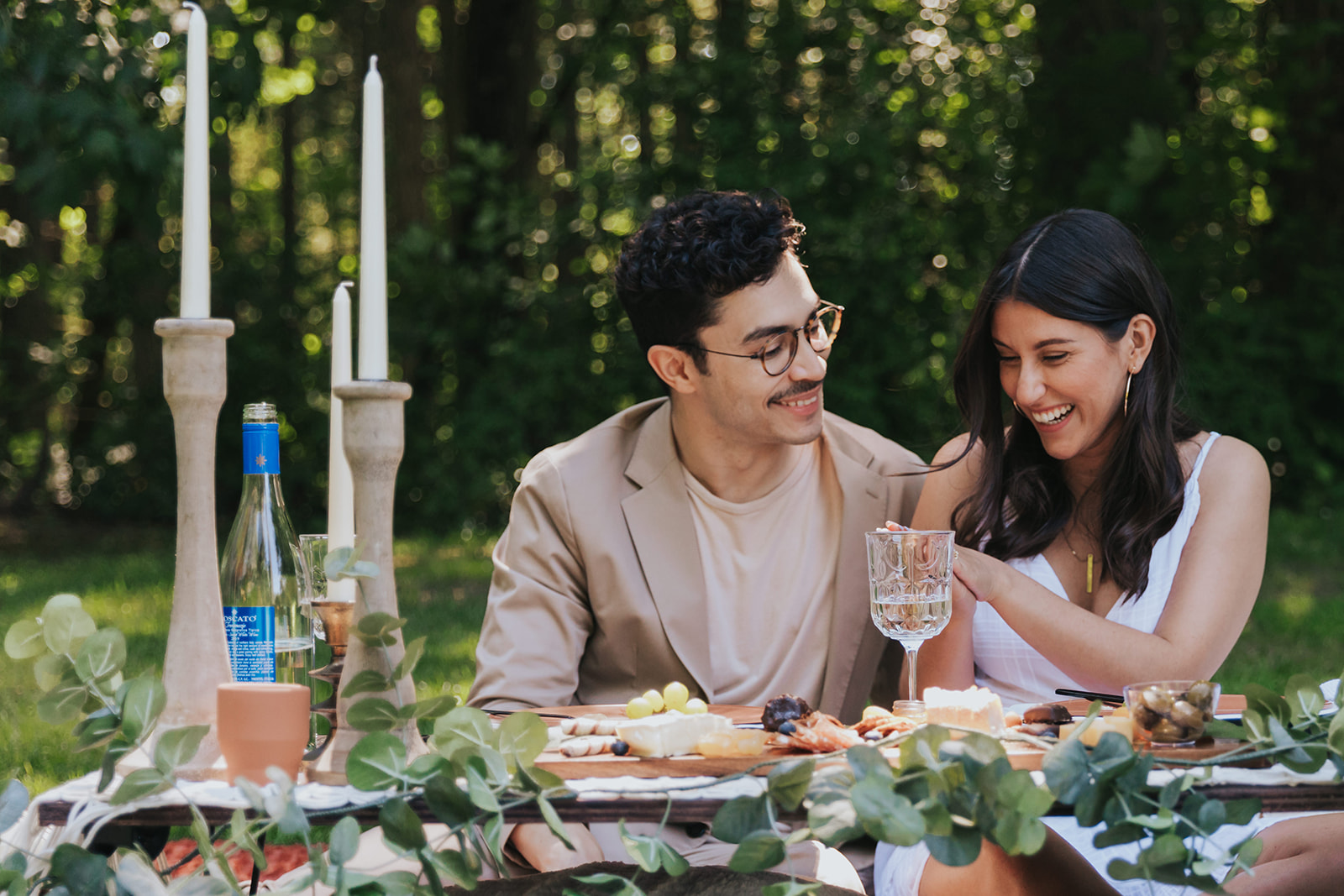 A couple smiles as they sit for a picnic during a surprise proposal