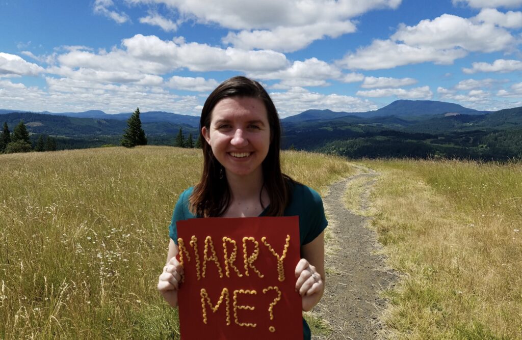 A woman is holding a red sign that reads "Marry Me?"