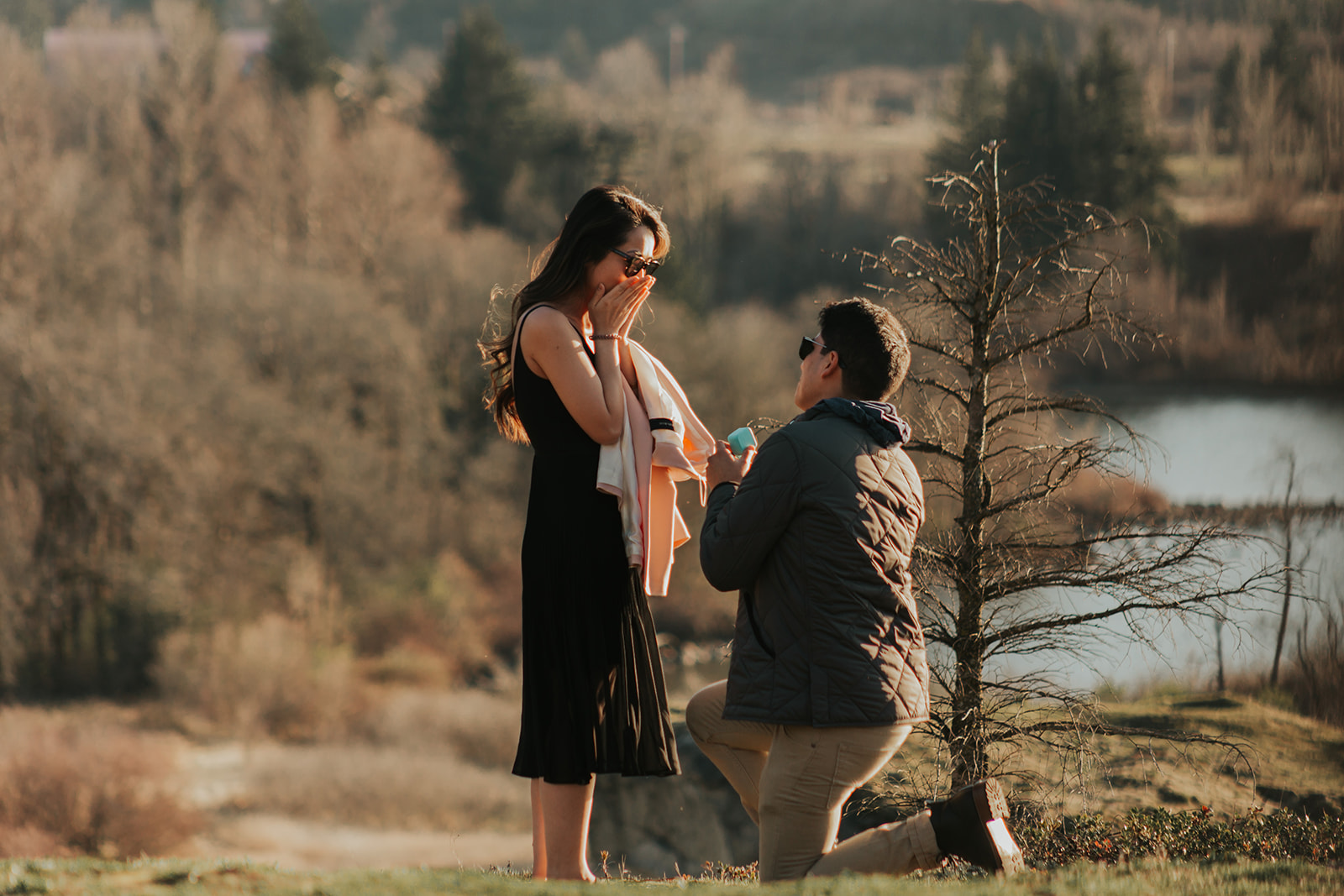 A man is kneeling down on one knee as he proposes with a ring to his partner.